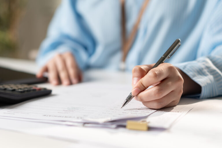 Businesswoman reviewing financial documents, tax paperwork, file folders, and business records on a laptop, representing accounting, document management, compliance, and office administration.